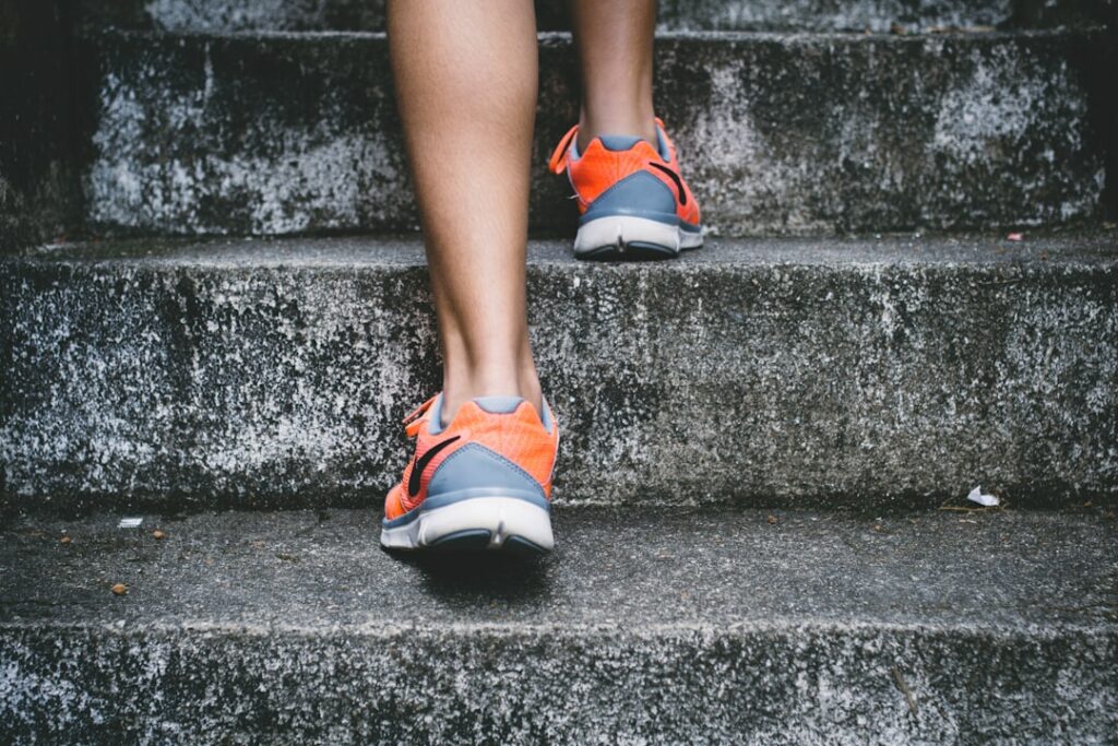 A person wearing orange and gray athletic shoes walks up a set of concrete steps. The focus is on their legs and shoes.